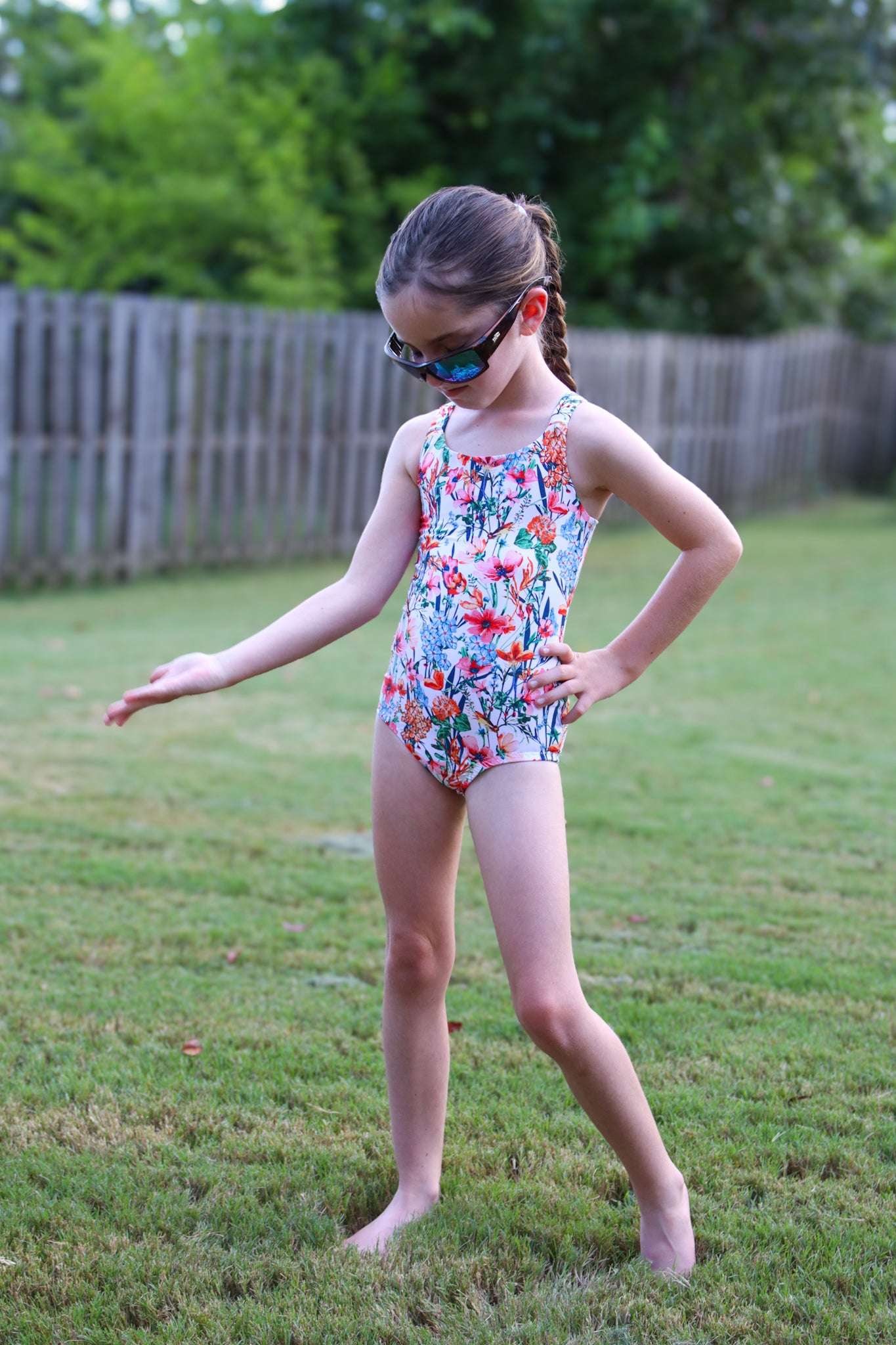 Young girl in a floral swimsuit standing on grass with sunglasses on