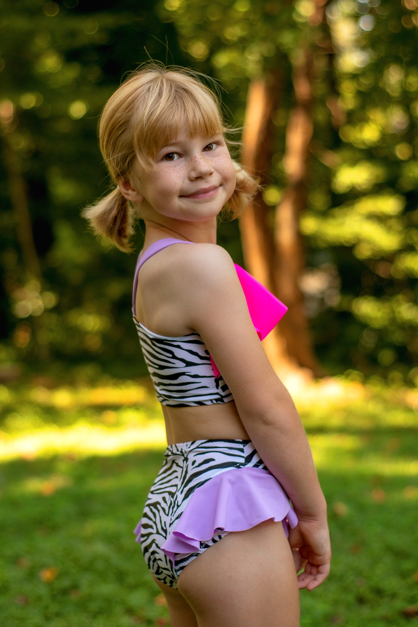 Young girl wearing a colorful two-piece swimsuit with zebra print and pink accents, standing outdoors.