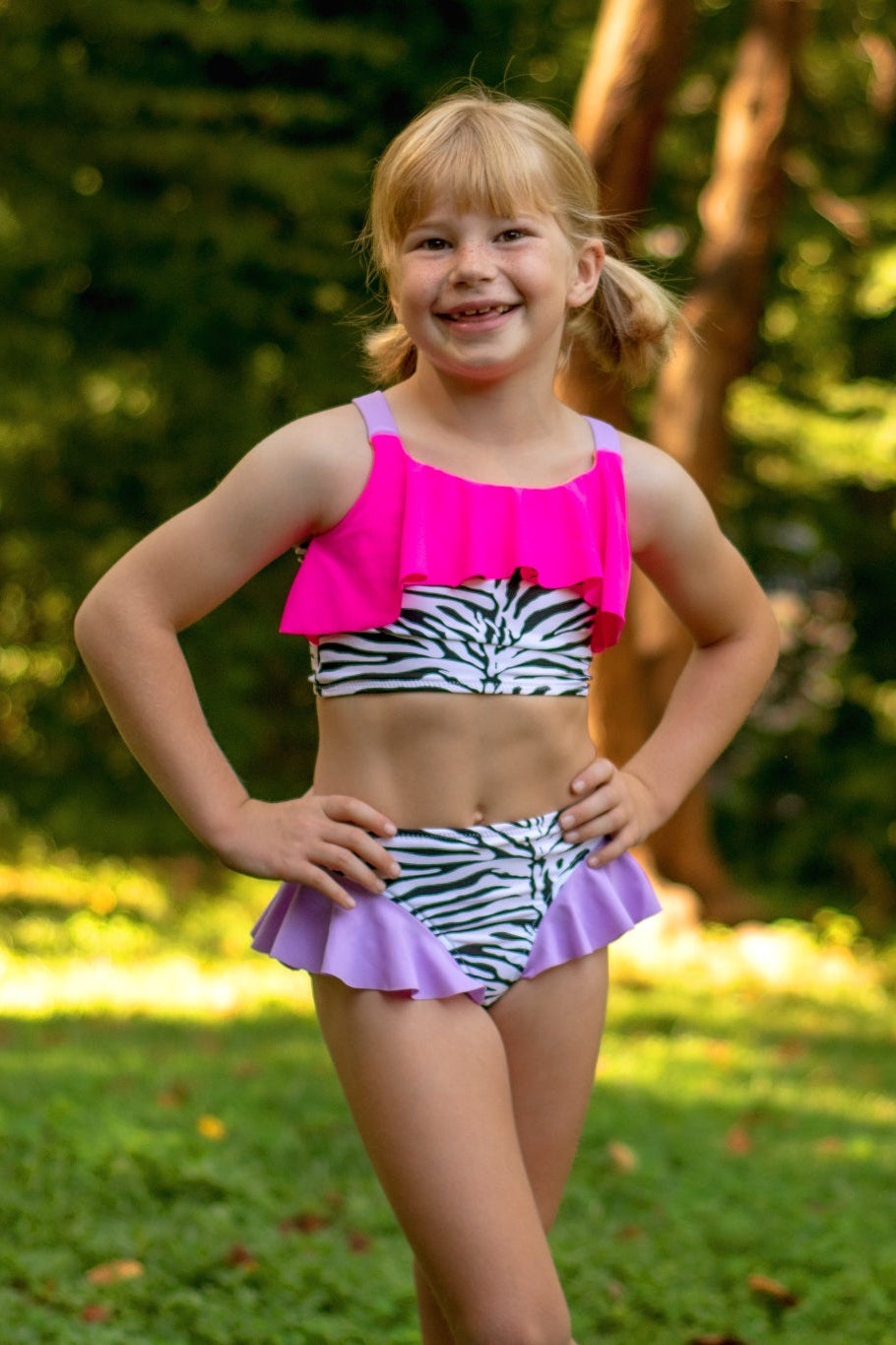 Young girl in a colorful swimsuit standing outdoors with greenery in the background