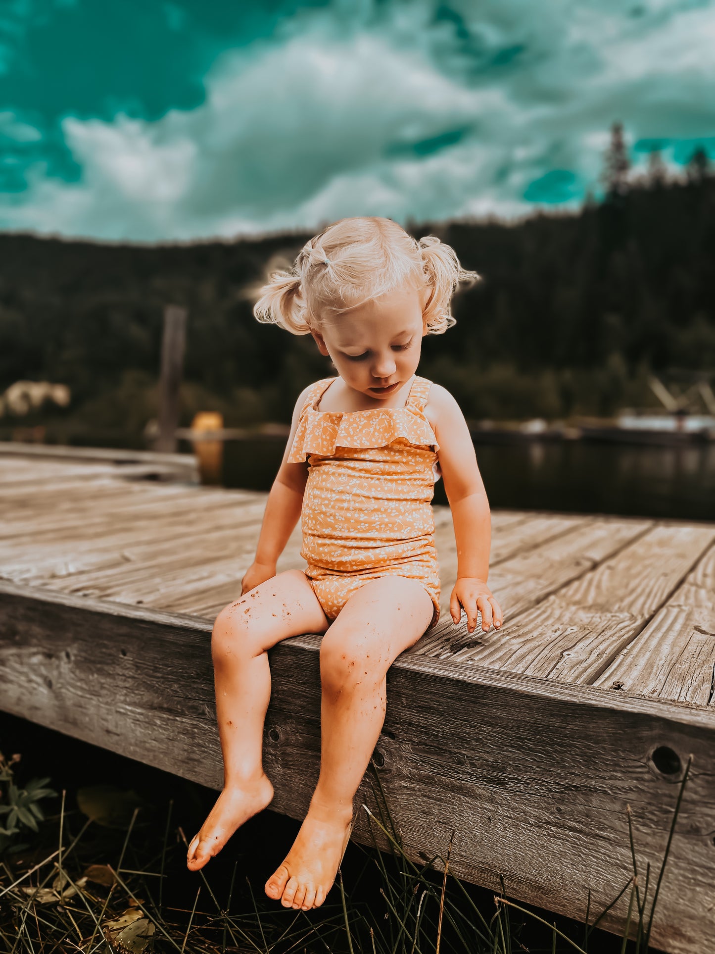 Child sitting on a wooden dock by a lake with mountains in the background