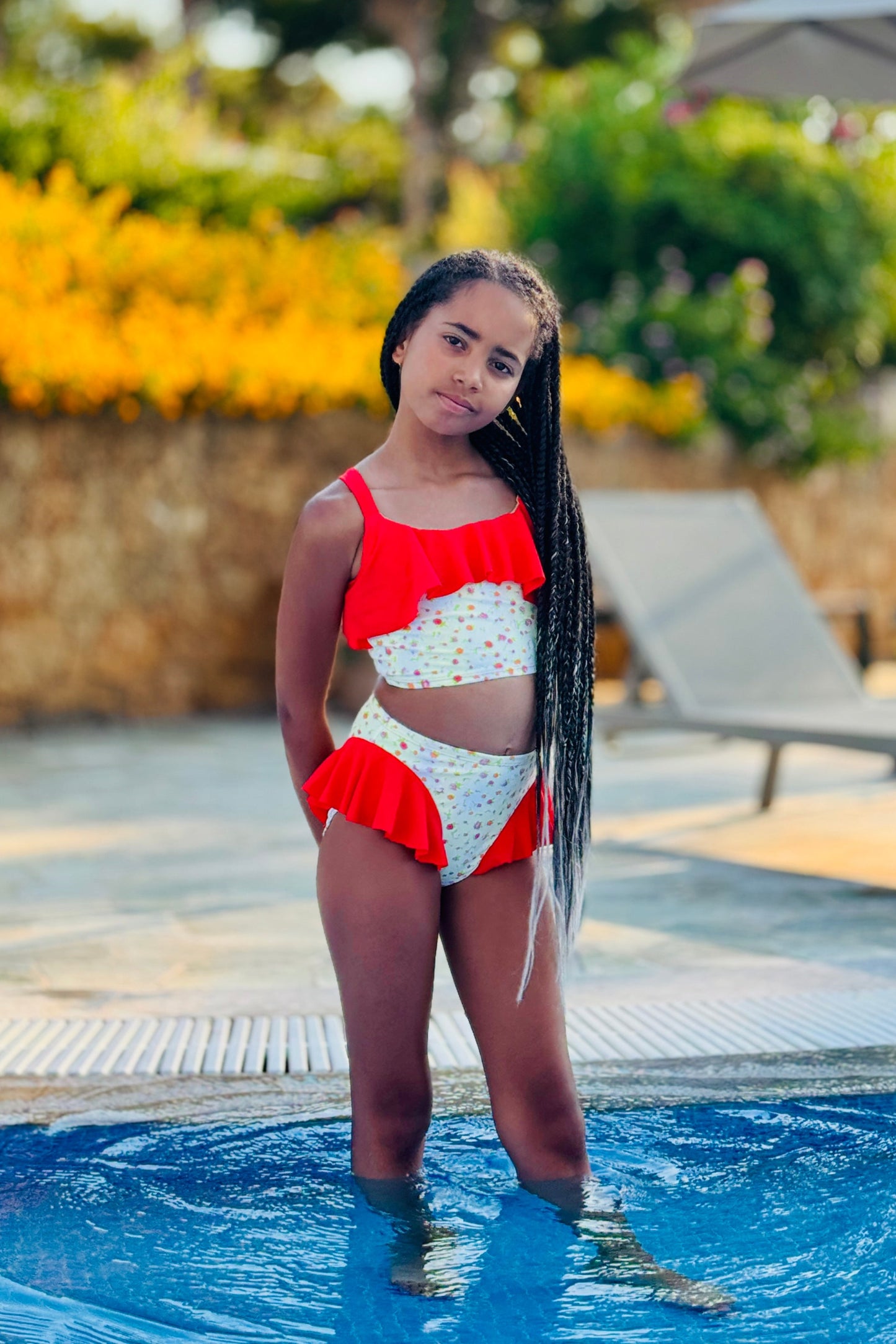 Young girl in a red and white swimsuit standing by a pool with palm trees in the background
