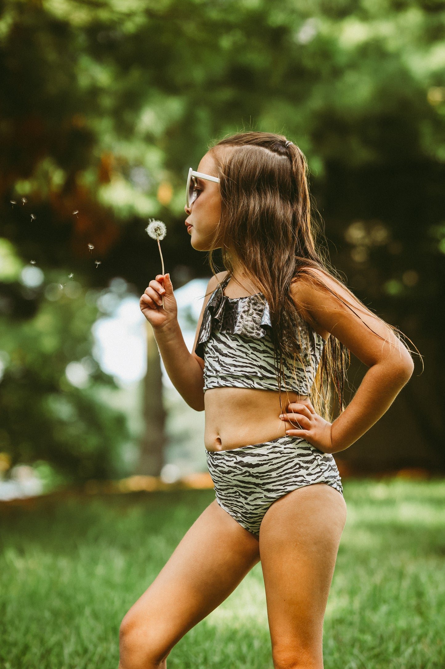 Young girl in a zebra print swimsuit holding a dandelion in a grassy outdoor setting