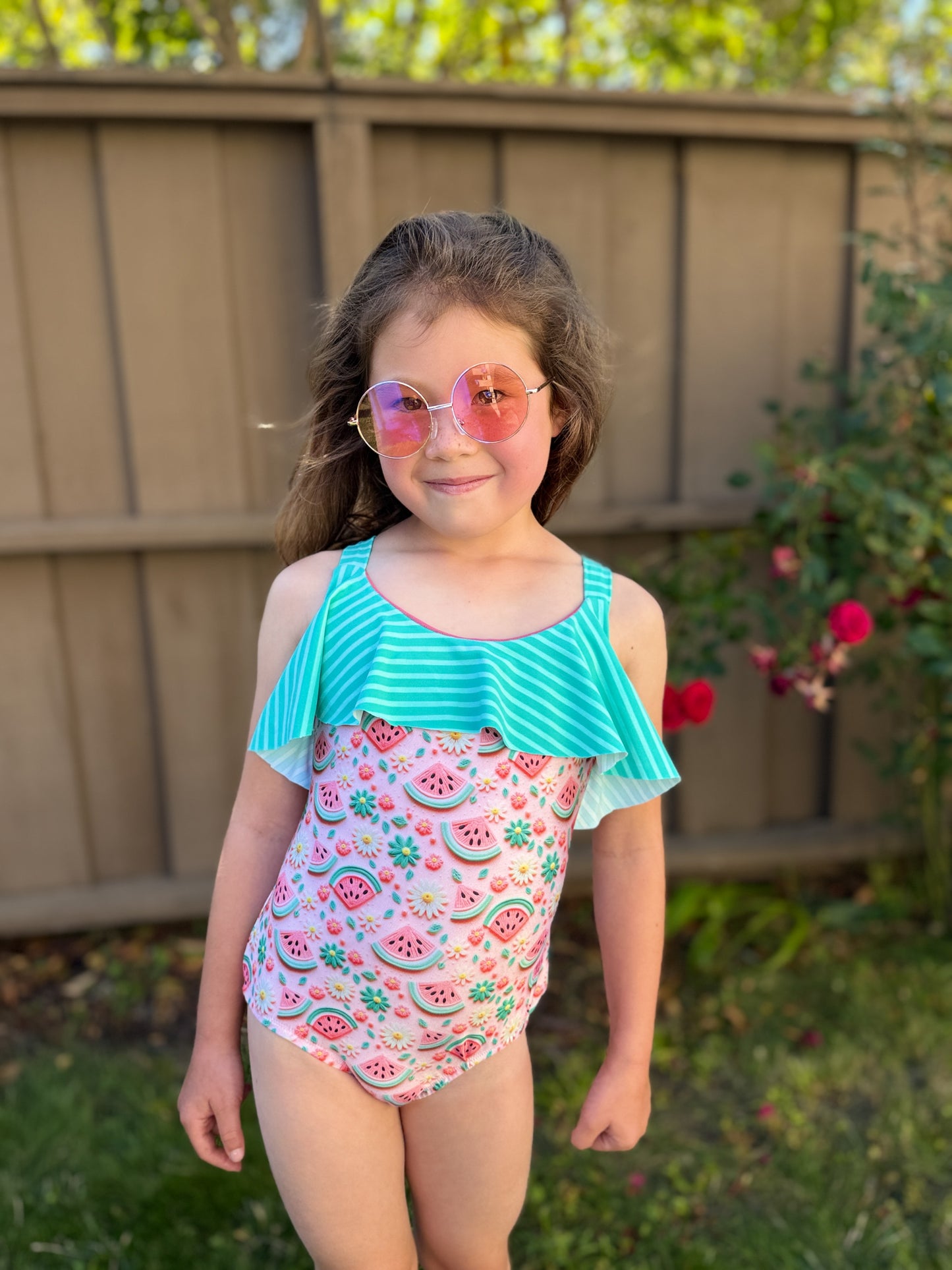 Young girl wearing a colorful swimsuit with a watermelon pattern outdoors.