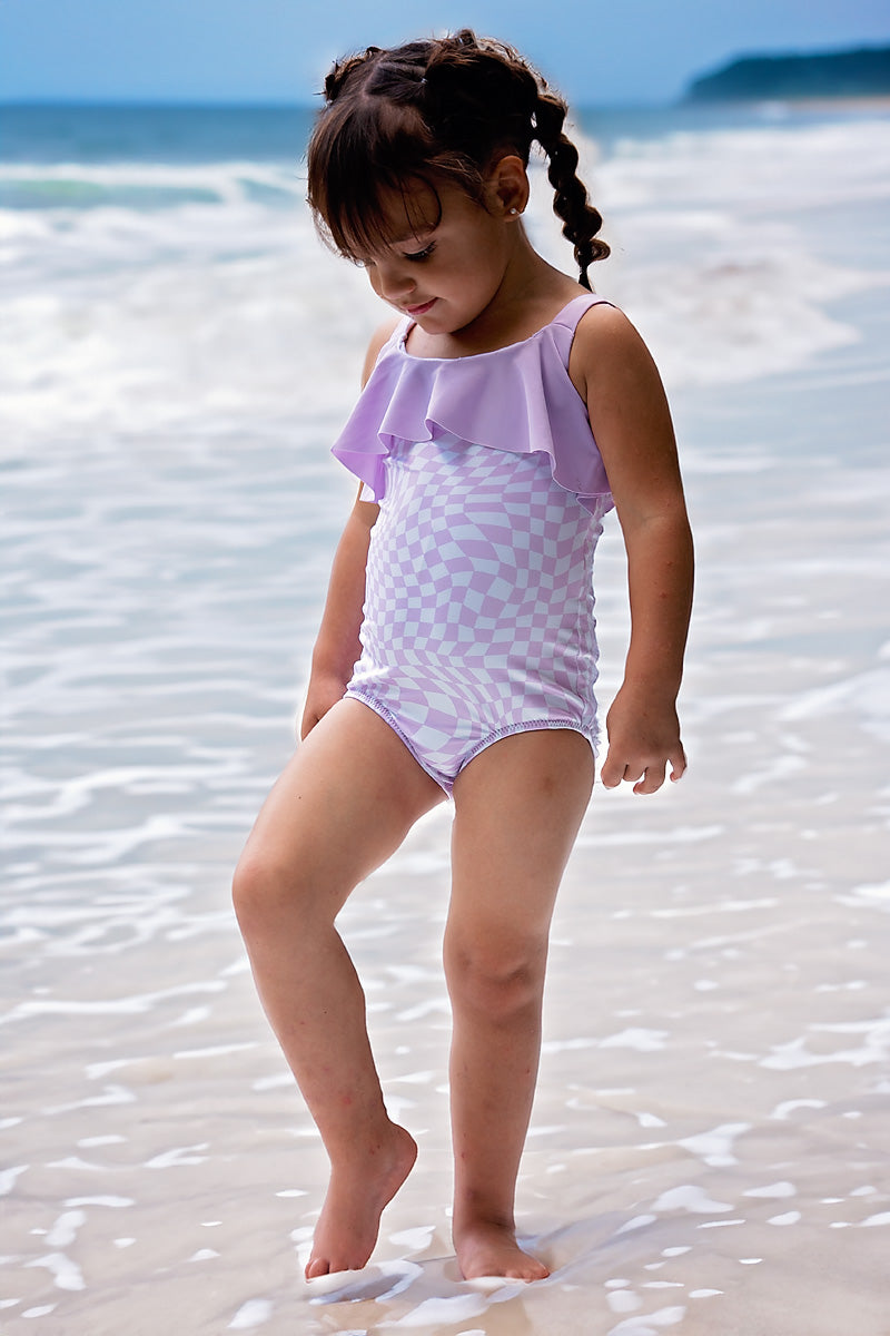 Young girl in a purple swimsuit standing on a sandy beach with ocean in the background