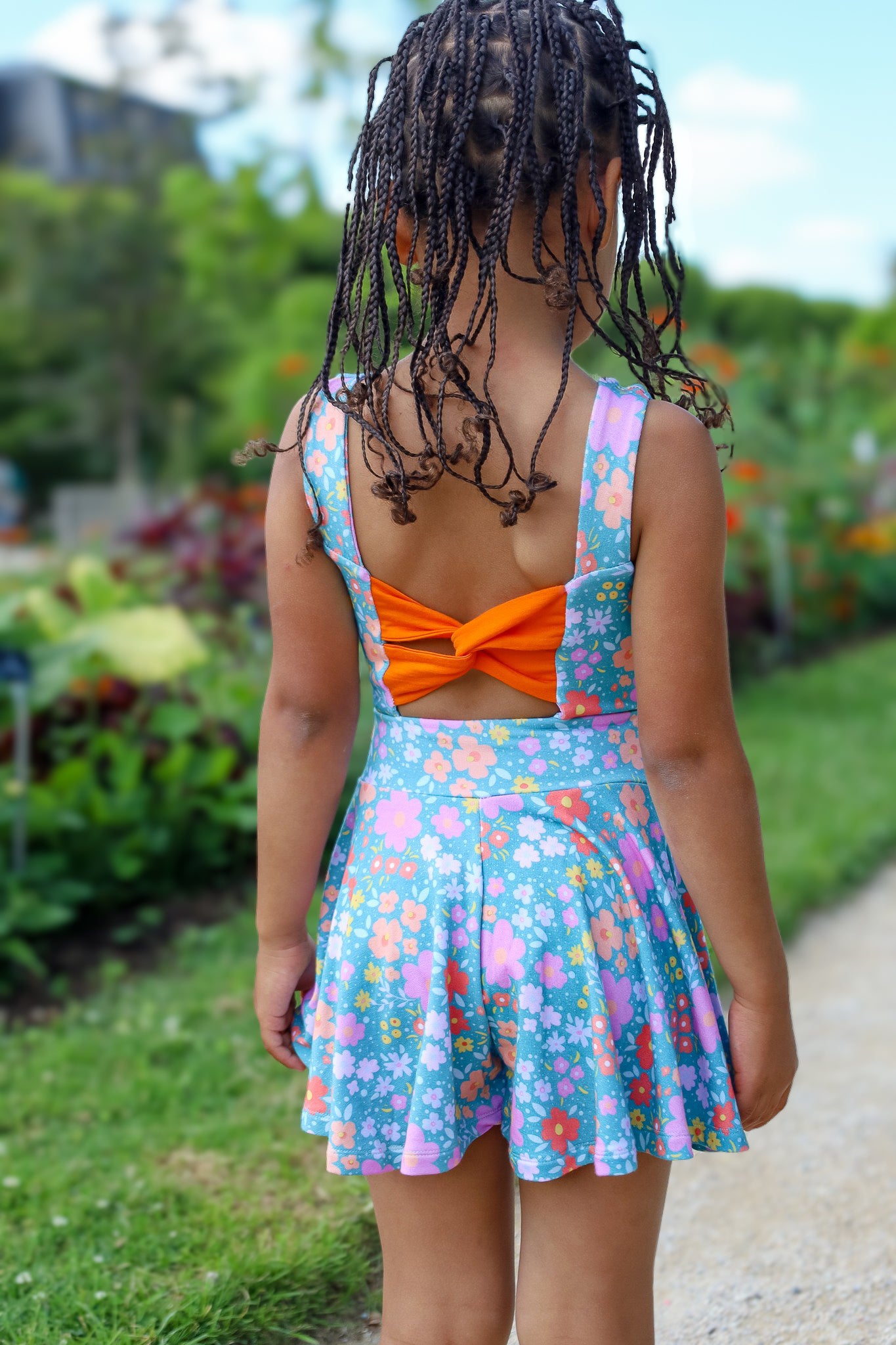 Child wearing a colorful dress with an orange bow in a garden setting