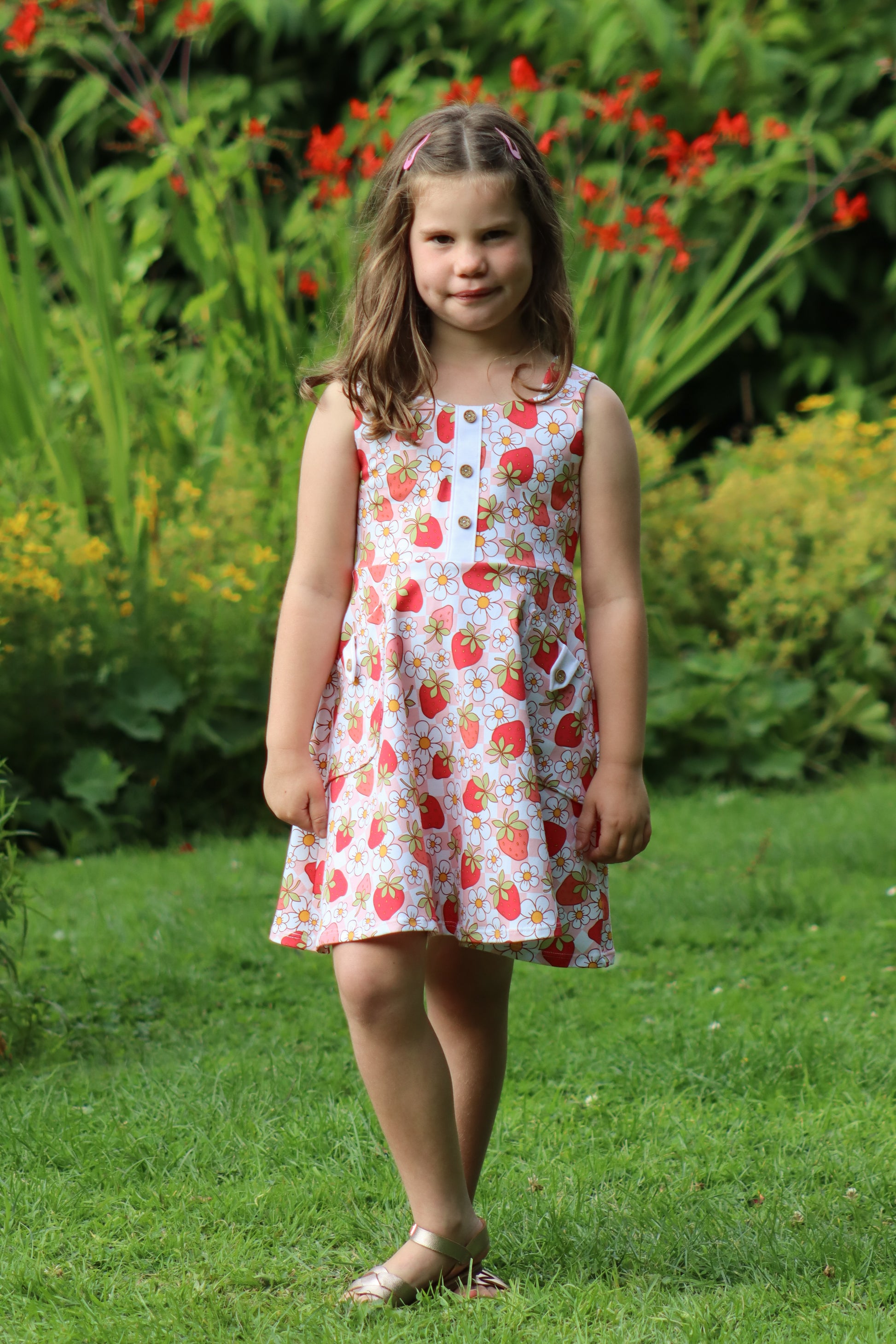 Young girl in a floral dress standing in a garden with greenery and flowers in the background