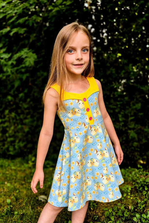 Young girl in a floral dress standing outdoors near a tree