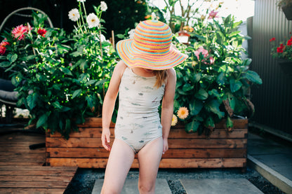 Person wearing a patterned swimsuit and colorful hat in a garden setting