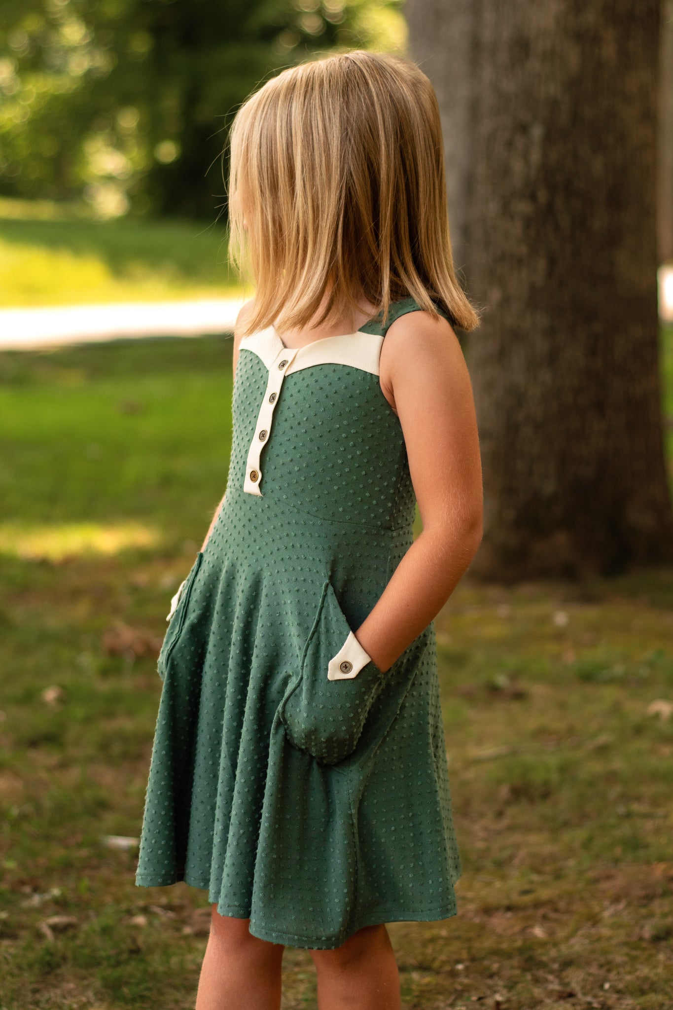 Young girl in a green dress standing outdoors near a tree. textured knit fabric dress with pockets