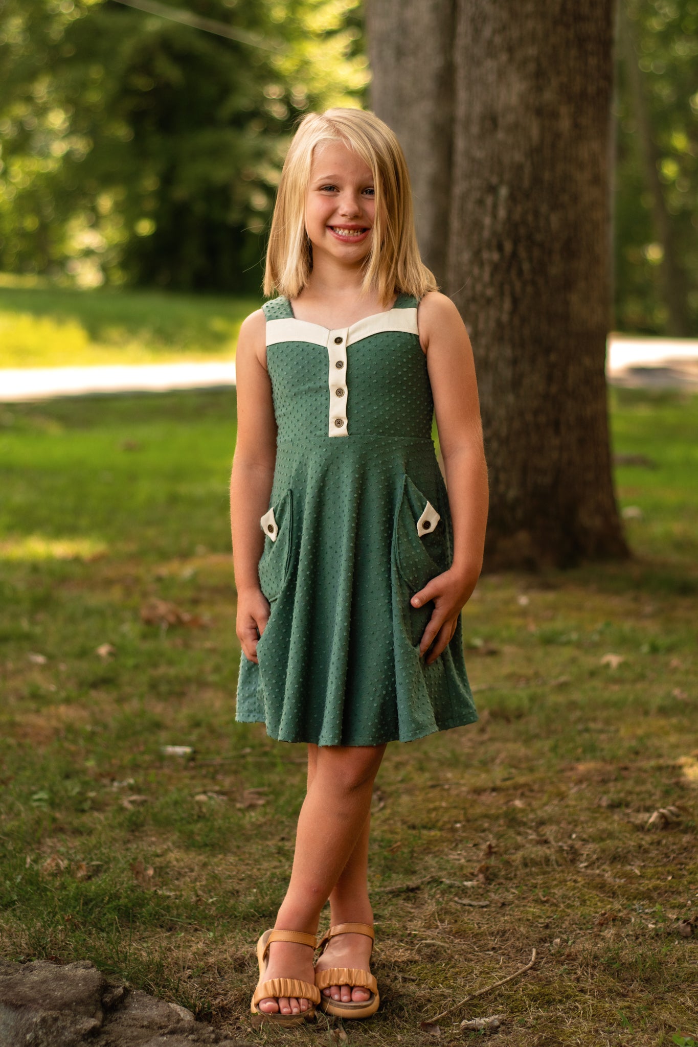 Young girl in a green dress standing outdoors near a tree