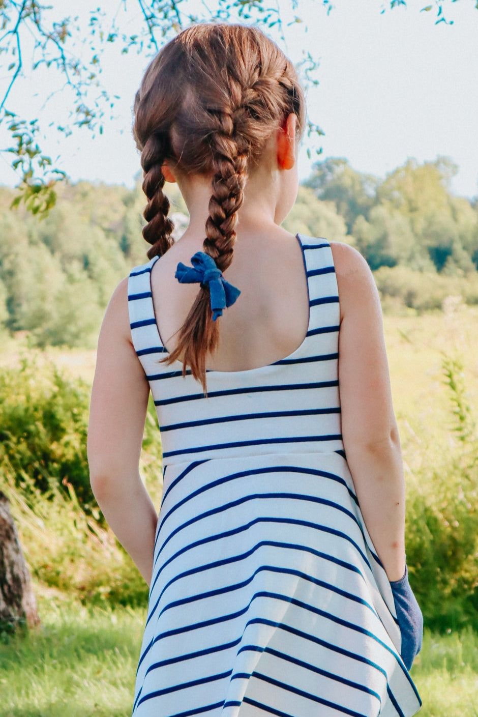 Girl in a striped dress standing in a grassy field with trees in the background