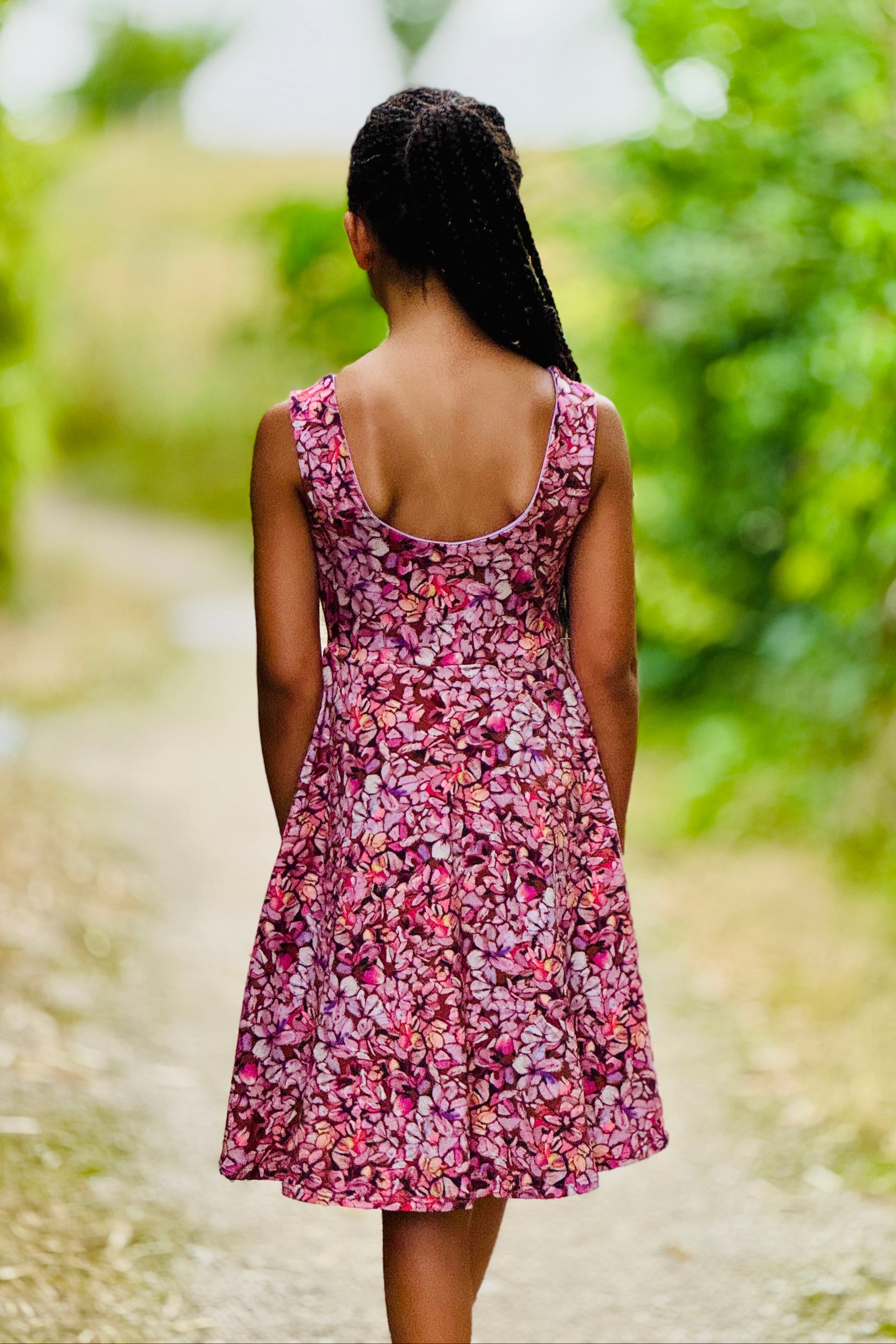Girl in a pink floral dress walking away on a path with greenery
