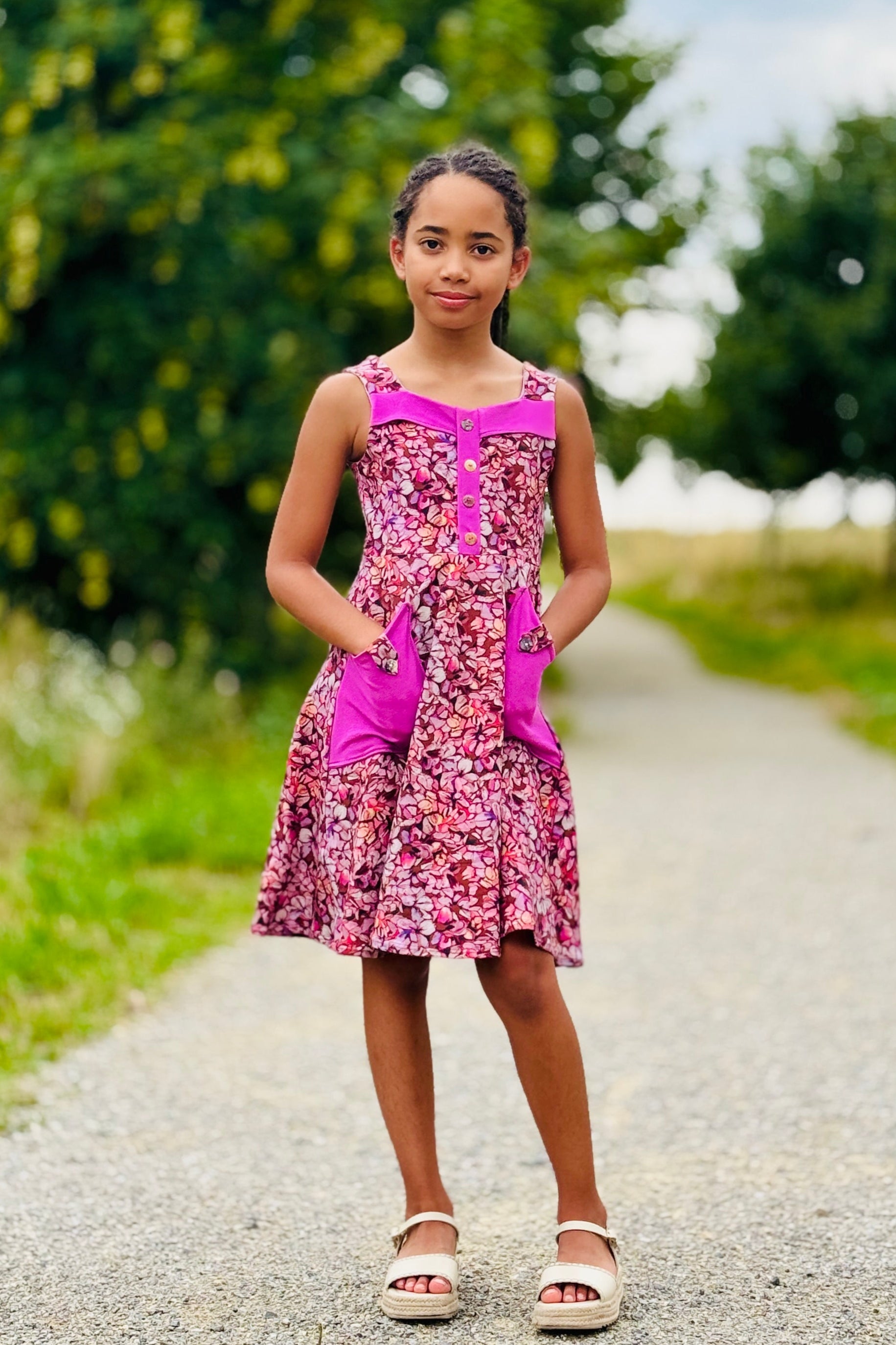Young girl in a pink dress standing on a gravel path with trees in the background