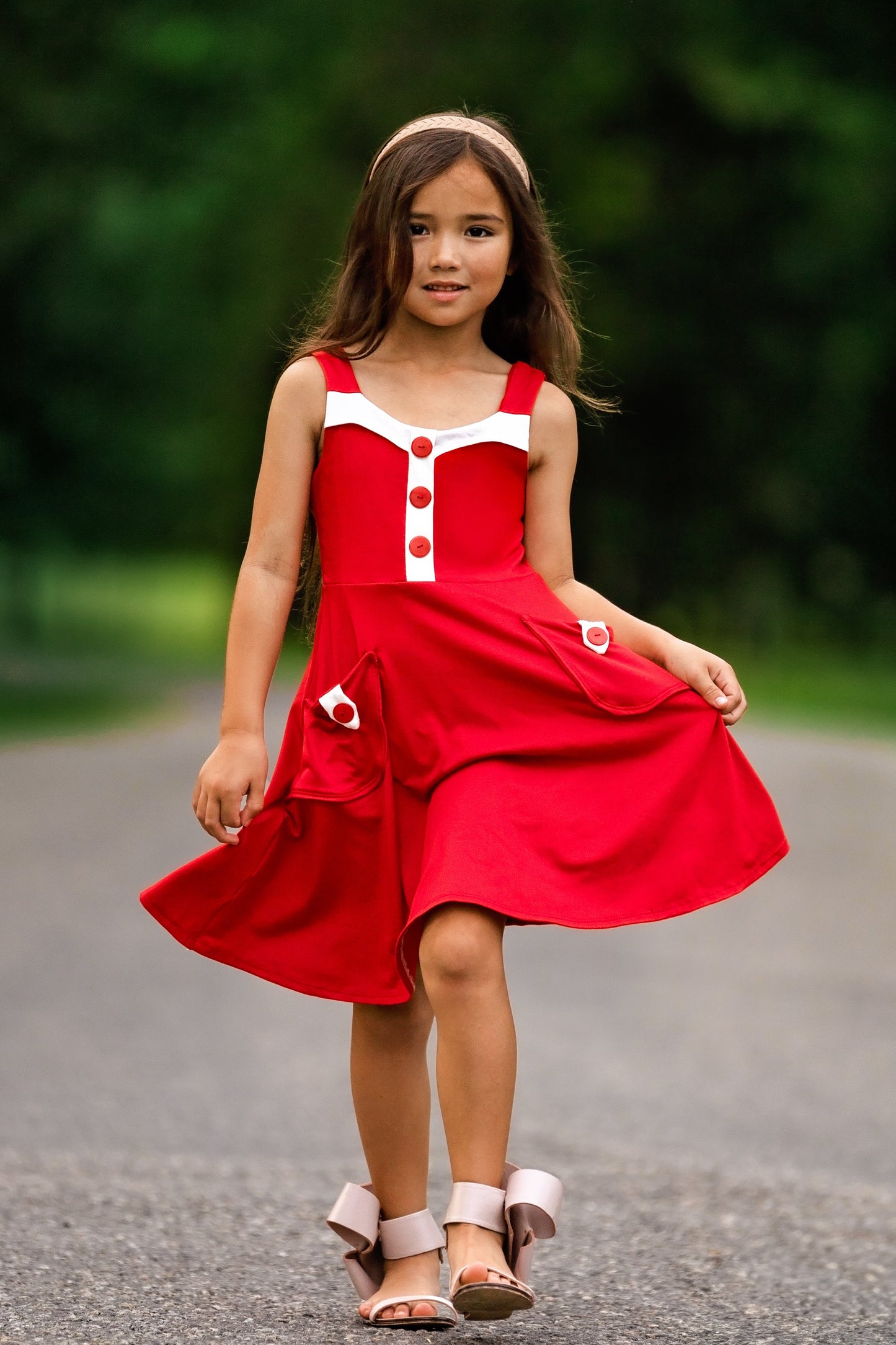 Young girl in a red dress standing on a road with greenery in the background