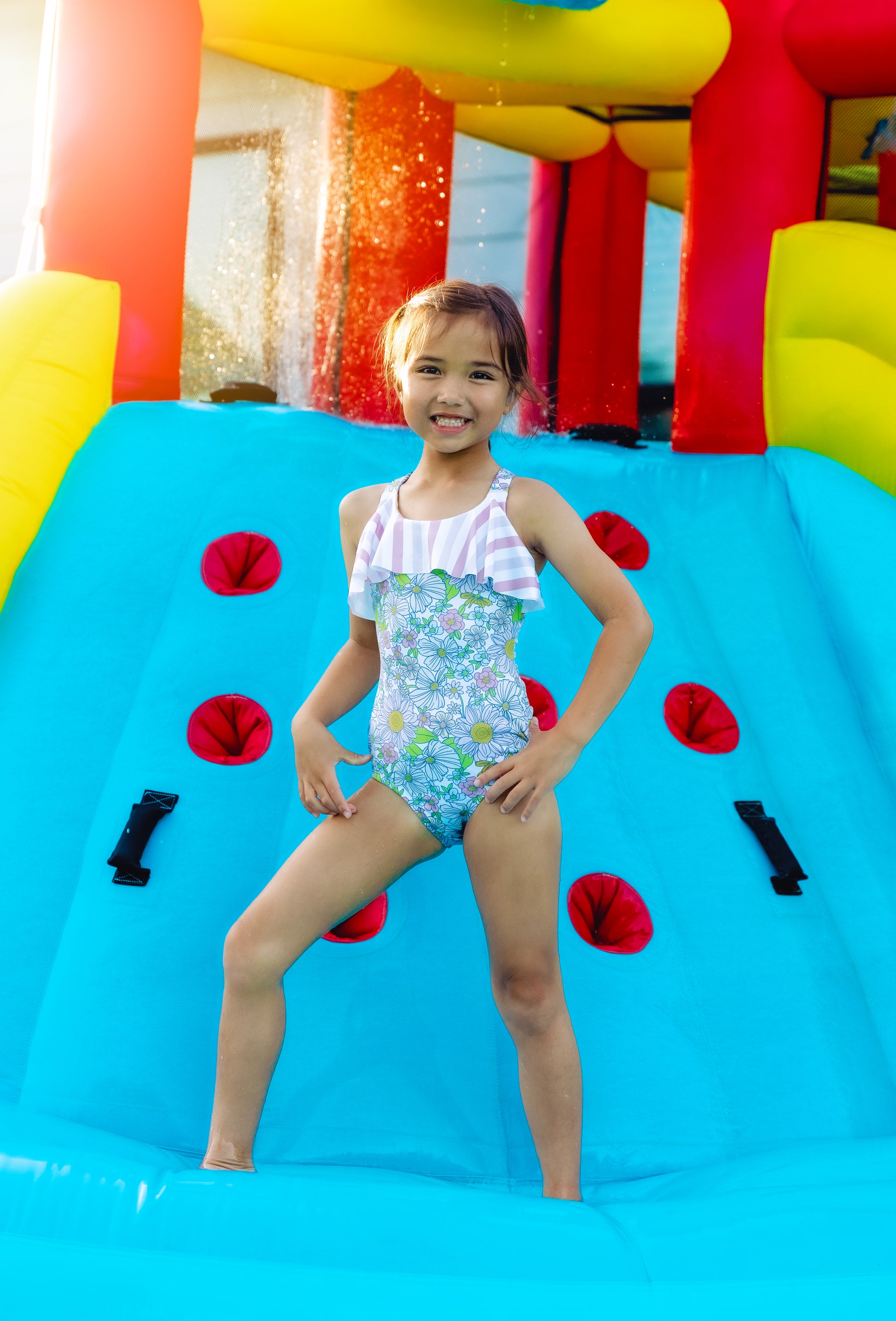 Young girl in a colorful swimsuit standing on a blue inflatable slide with red and black decorations.