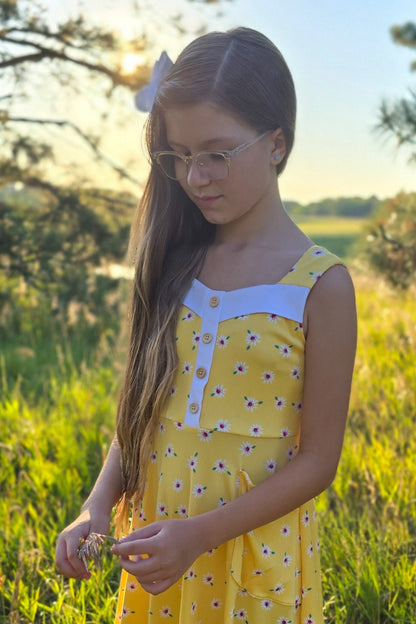 Young girl in a yellow dress standing in a grassy field with trees in the background