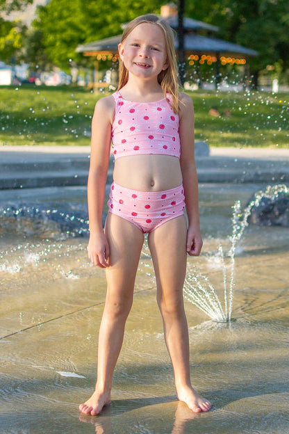 Young girl in a pink swimsuit standing in a fountain with water splashing around her.