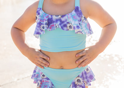 Child wearing a two-piece swimsuit with floral top and bottom on a beach.