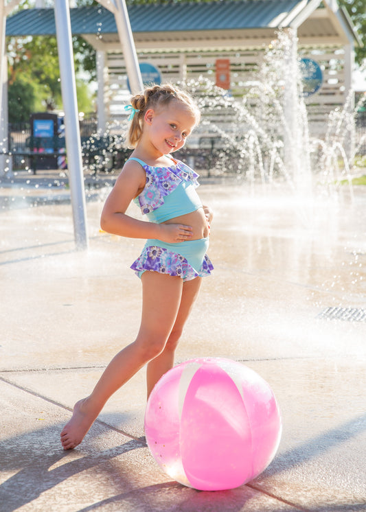 Young girl in a colorful swimsuit standing next to a pink beach ball at a water park.