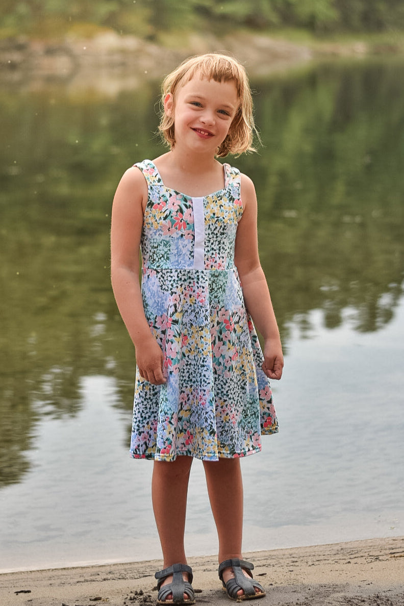 Young girl in a floral dress standing by a lake with trees in the background